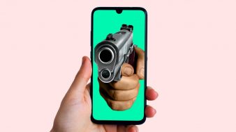 Uma mão segura um celular. No celular aparece a imagem de uma pessoa apontando uma arma.